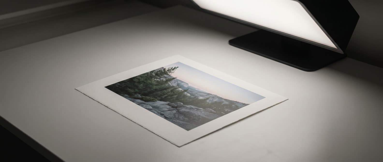 Fine art-print under en D50-bedömningslampa, mjuk skugga på matt bordsyta